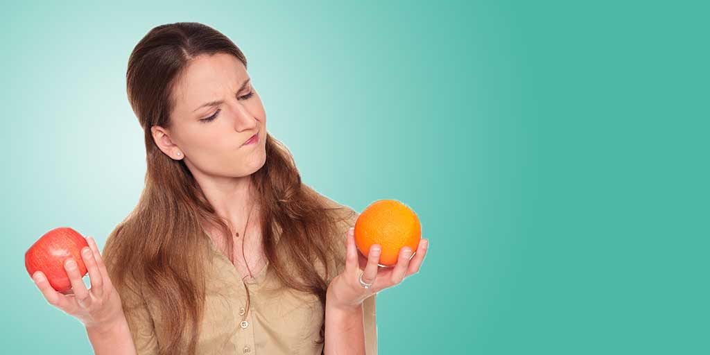 Woman comparing an apple and an orange, illustrating decision-making in choosing between different options, relevant to discussions on key man insurance and business protection services.